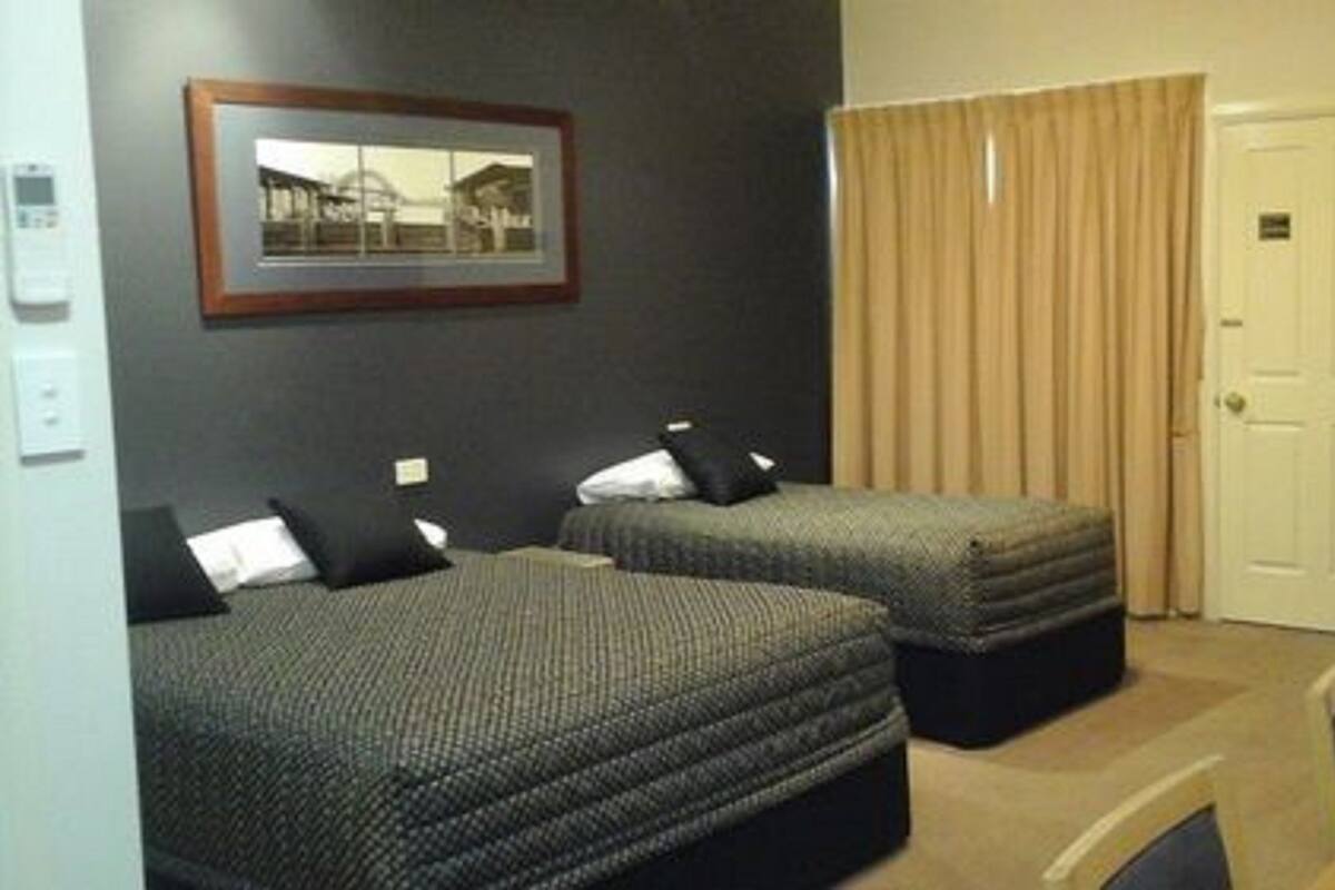 Habitación de hotel con dos camas, un cuadro en la pared, una puerta y una cortina.