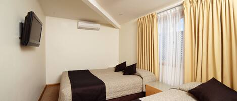 Habitación de hotel con dos camas, un televisor montado en la pared y un ventanal con cortinas.