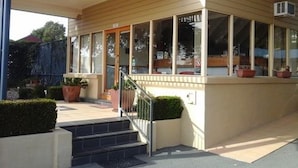 A modern building with a covered entrance, steps leading up to a door, and potted plants near the entrance. - Willows Motel Goulburn (Goulburn)