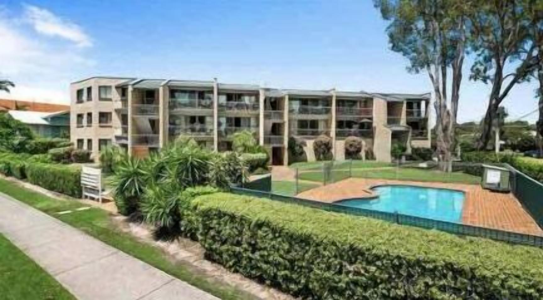 A modern multi-story hotel with a swimming pool and well-maintained gardens.