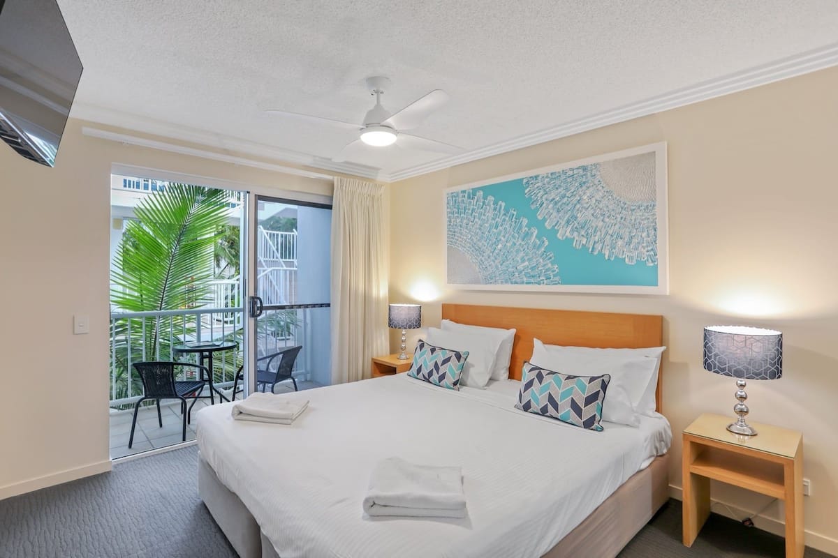 Une chambre d’hôtel avec un grand lit, deux tables de chevet, un ventilateur de plafond et un balcon avec des meubles d’extérieur.