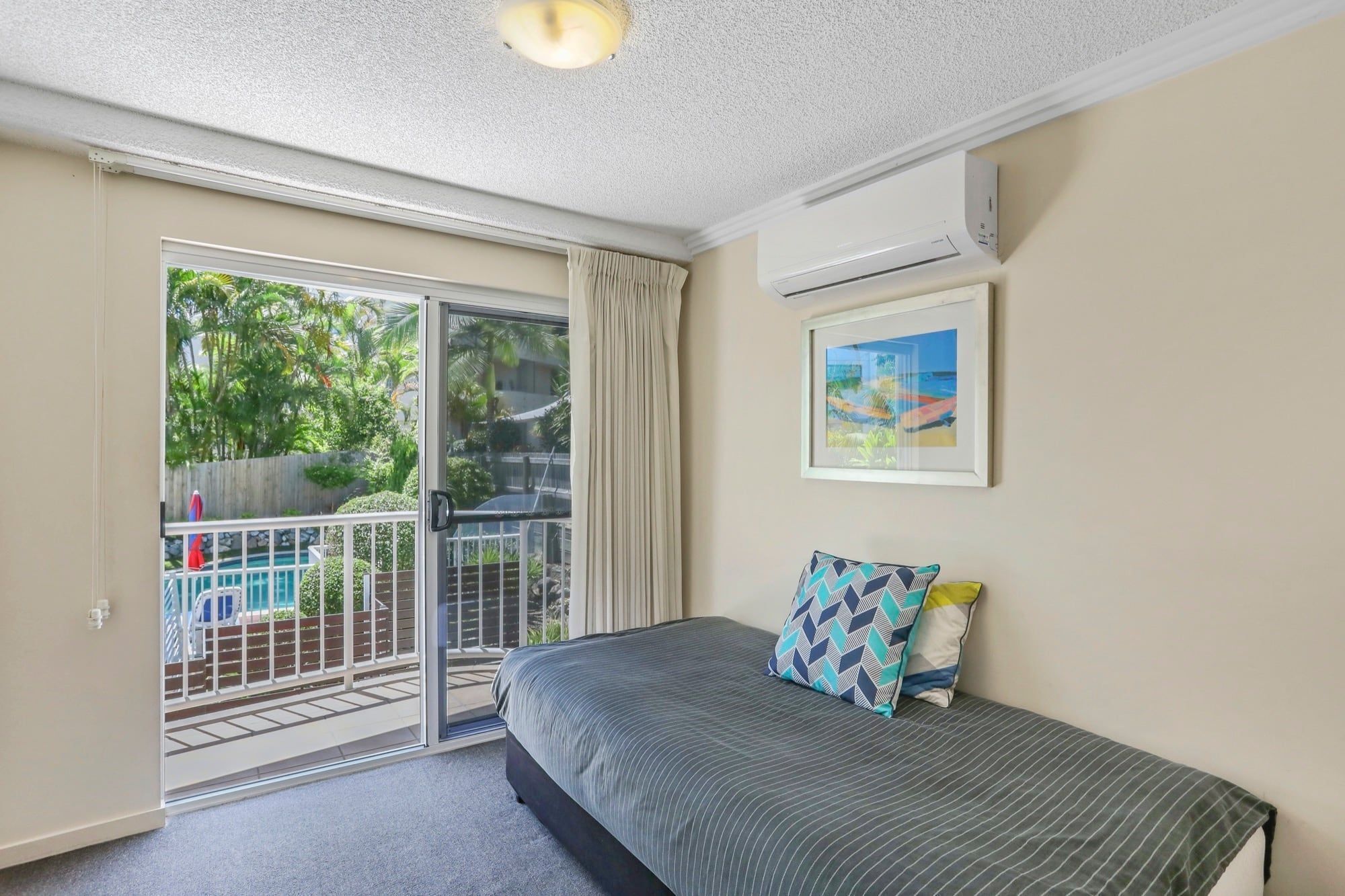 Un dormitorio con una cama, una ventana con cortinas, un equipo de aire acondicionado y un cuadro en la pared.