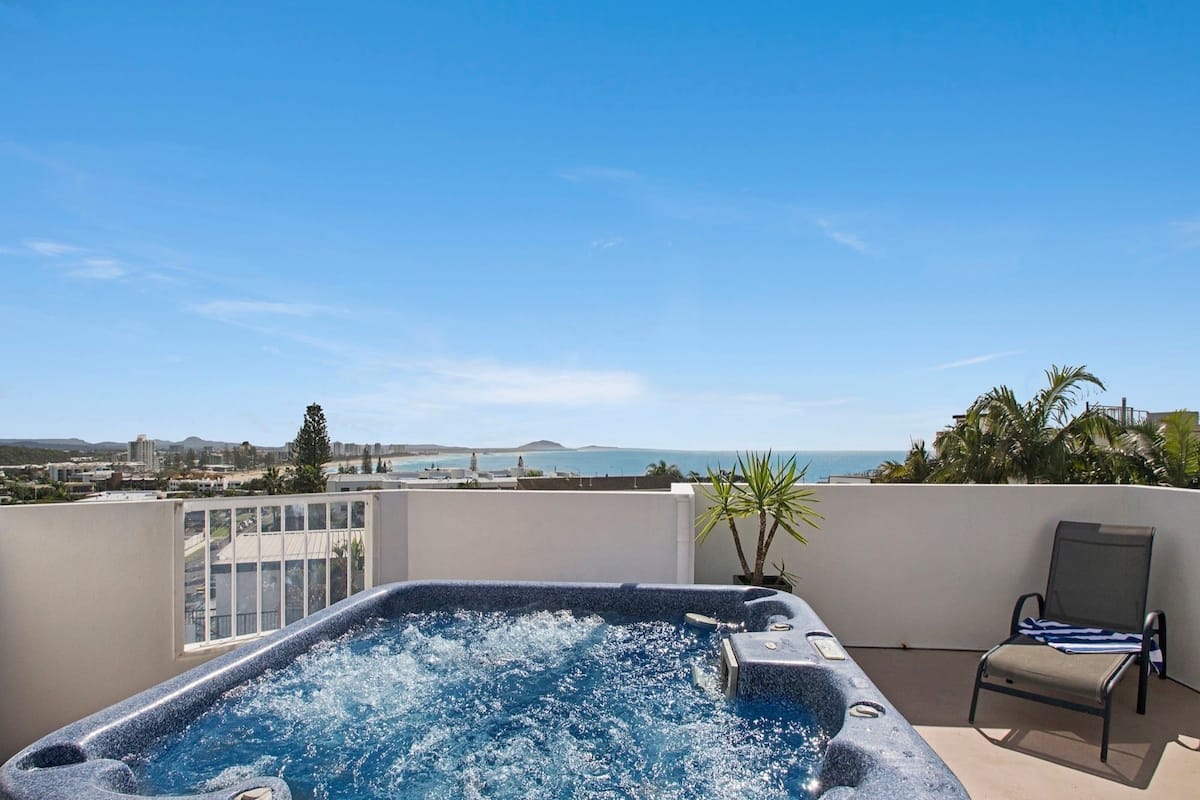 Un jacuzzi sur un toit-terrasse offrant une vue dégagée sur l’océan et le paysage urbain.
