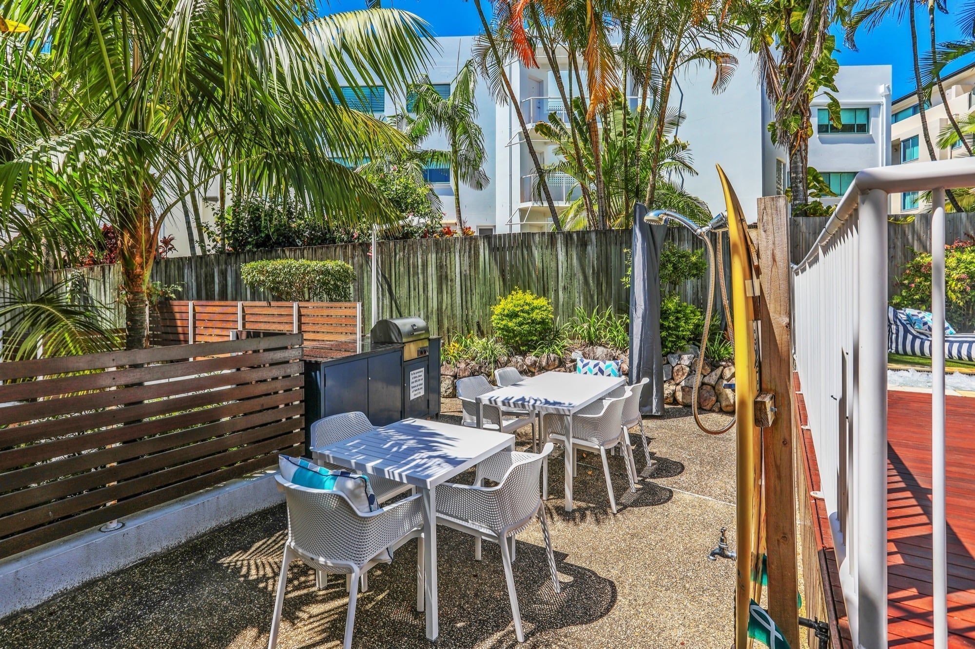 An outdoor patio with a wooden fence, a grill, and a seating area with tables and chairs.