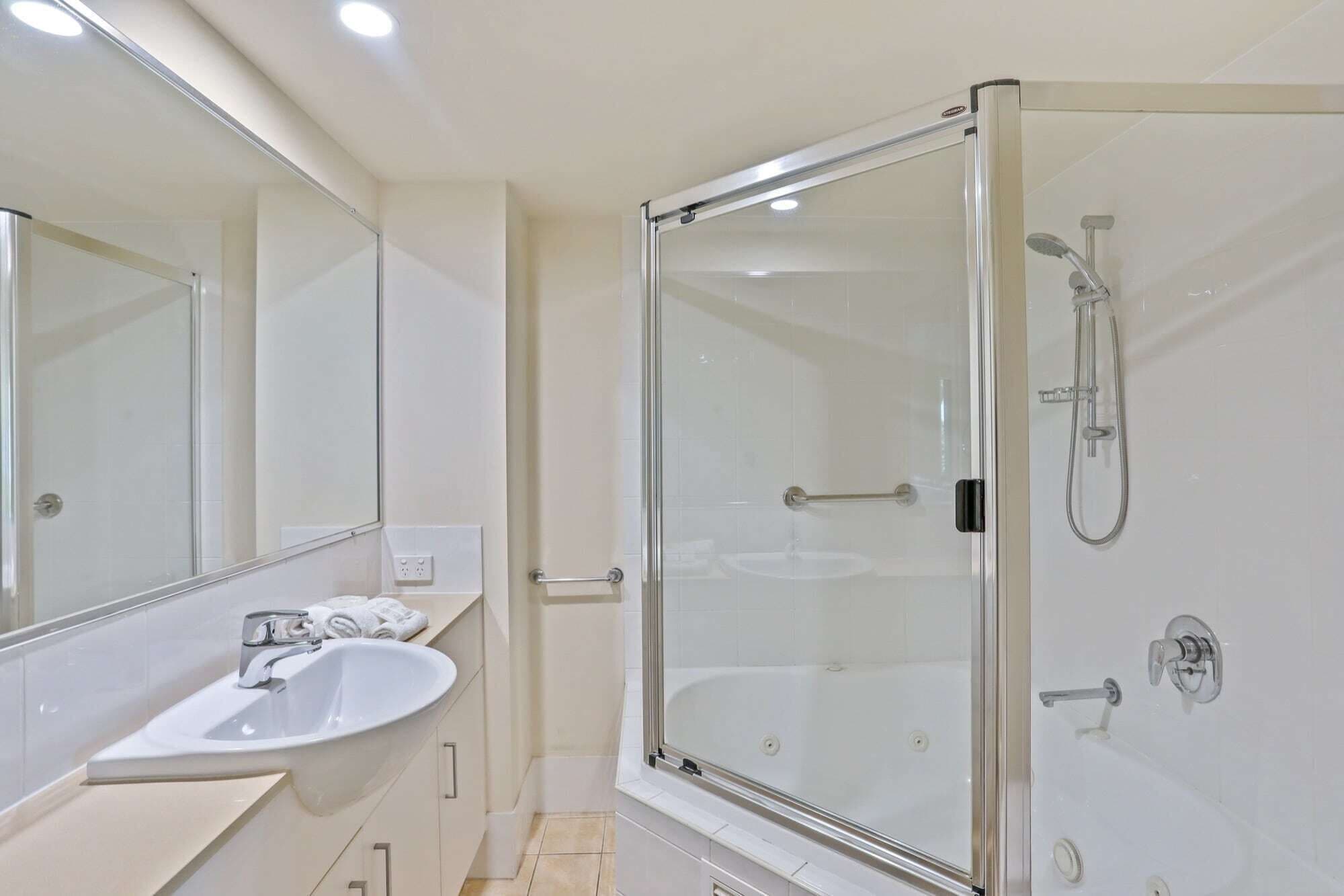 Un bany modern amb dutxa de vidre, un lavabo blanc i un mirall gran.