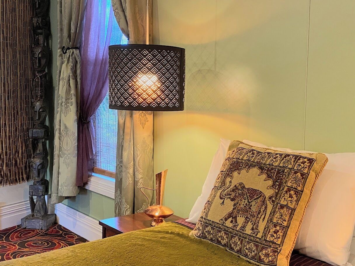 A room with a bed, a lamp, a window with curtains, and a decorative wall piece.