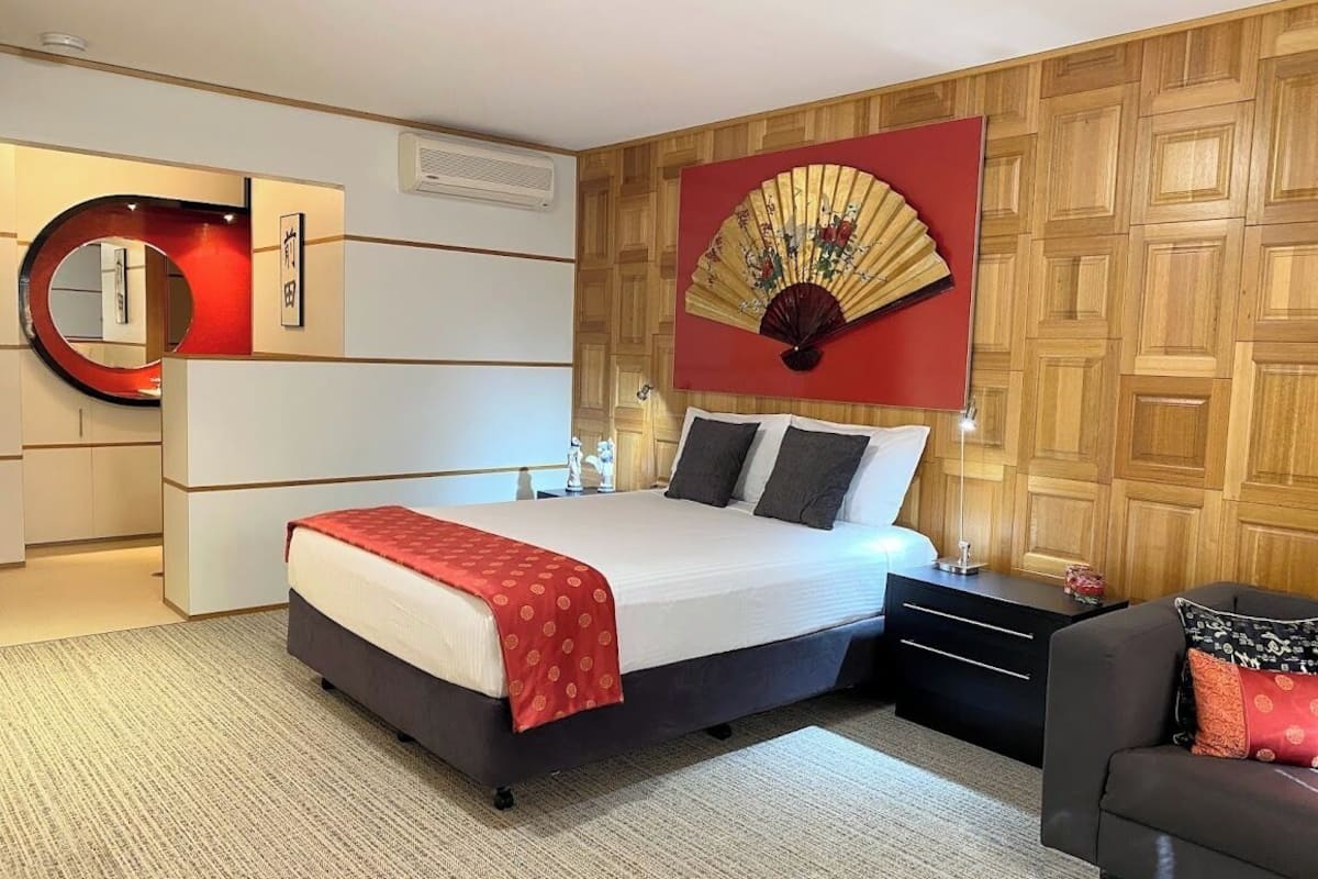 Une chambre d’hôtel moderne équipée d’un lit, de tables de chevet, d’un miroir, d’un ventilateur et d’un canapé.