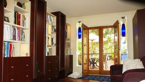 A room with a wooden bookshelf, a sofa, and a door leading to an outdoor patio with a table and chairs.
