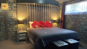 A bedroom with a large bed, a nightstand, a lamp, and a stone wall.