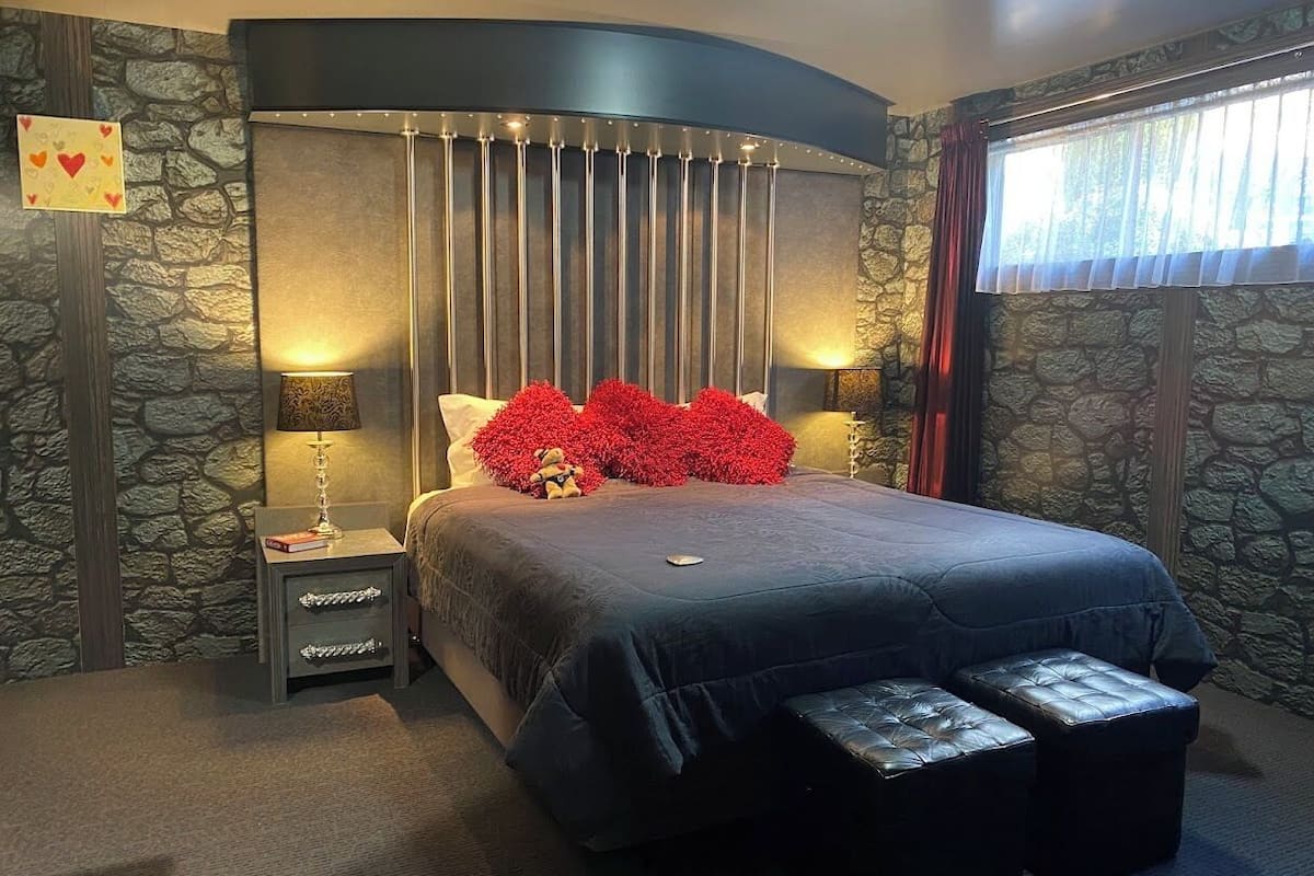 Une chambre avec un grand lit, une table de chevet, une lampe et un mur en pierre.