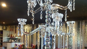 A chandelier with multiple crystal tiers and hanging crystals, surrounded by disco balls and a bar area with shelves of bottles.