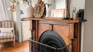 A living room with a fireplace, a wooden chair, and a large mirror. - Woolrich Historic Garden Cottage (Olinda)
