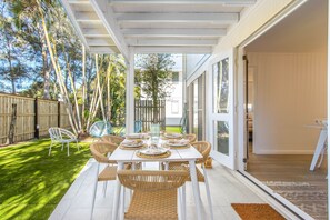 A patio with a table set for four, surrounded by wicker chairs, a wooden fence, and a grassy area. - Hastings Cove Waterfront Holiday Apartments (Hastings Point)