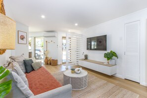 A modern living room with a sofa, coffee table, and TV. - Hastings Cove Waterfront Holiday Apartments (Hastings Point)
