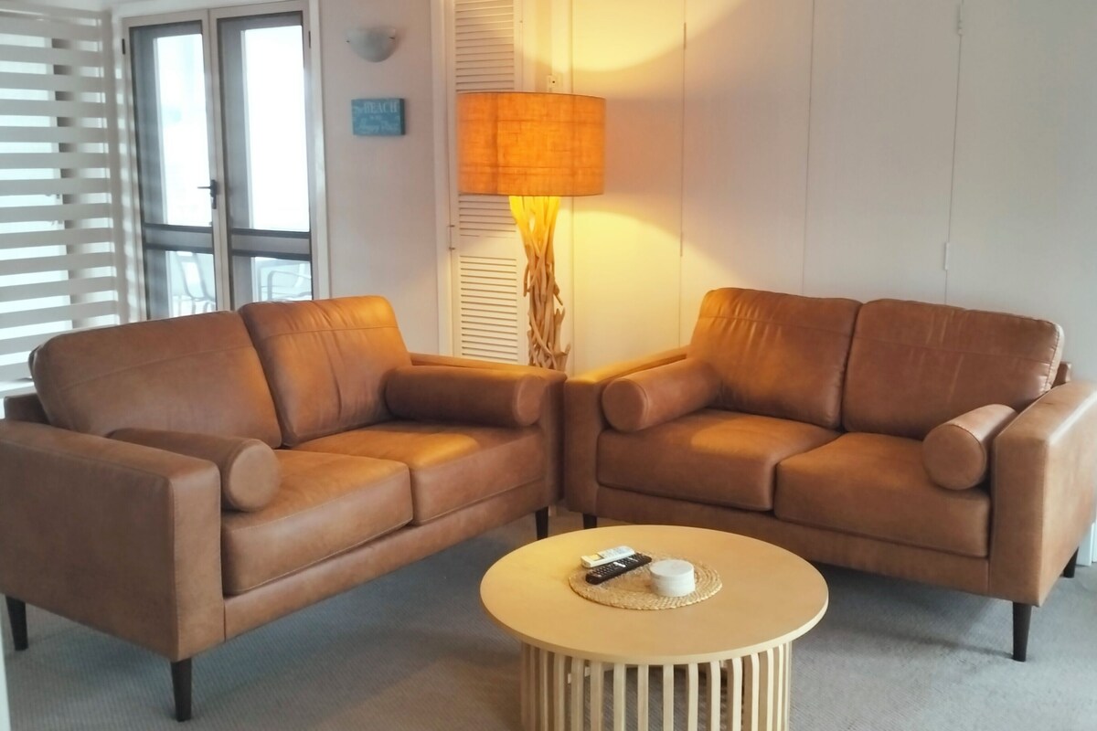 A living room with two brown leather sofas, a round coffee table, and a floor lamp.