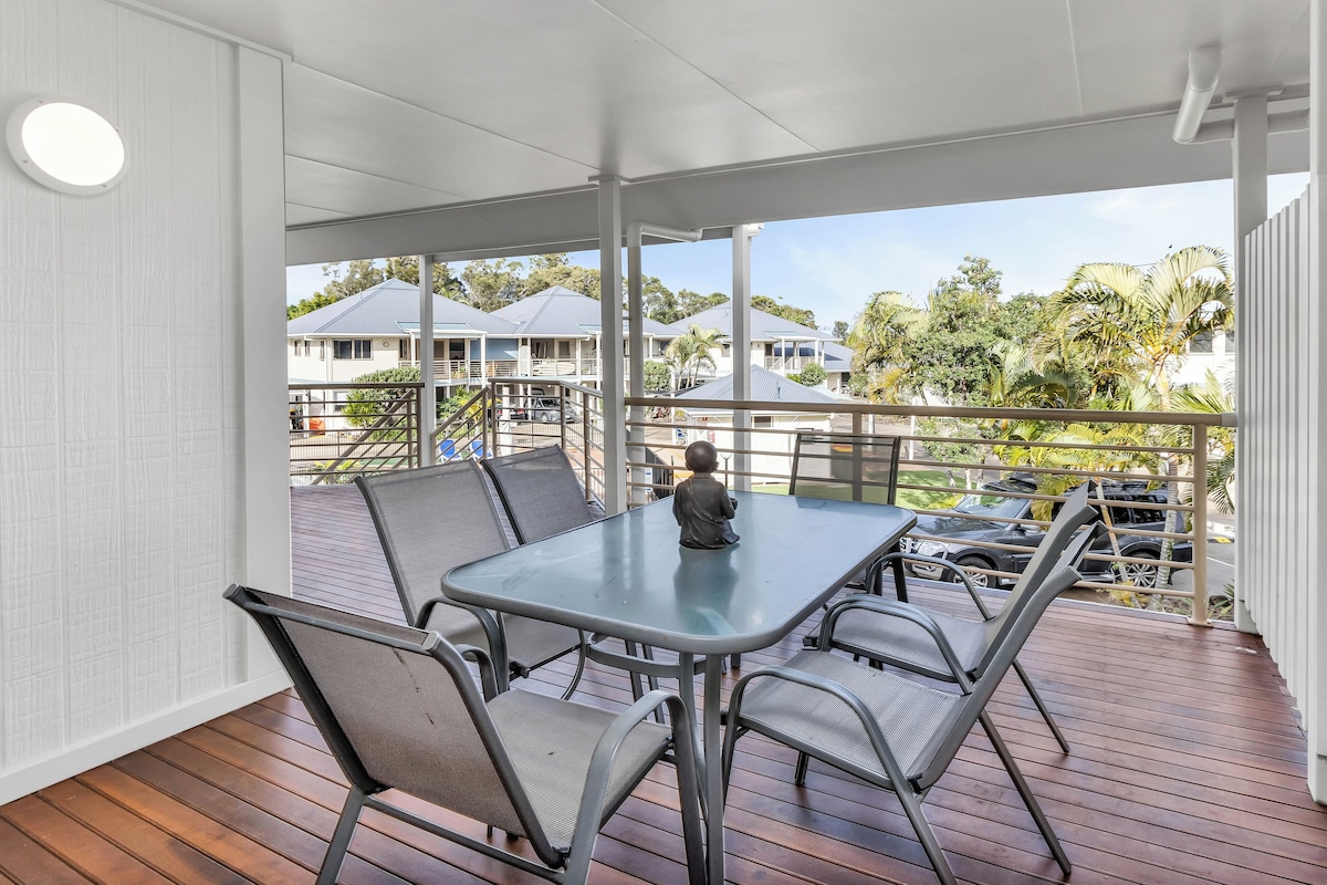 A covered outdoor area with a table and chairs, a view of houses and palm trees, and a white ceiling.