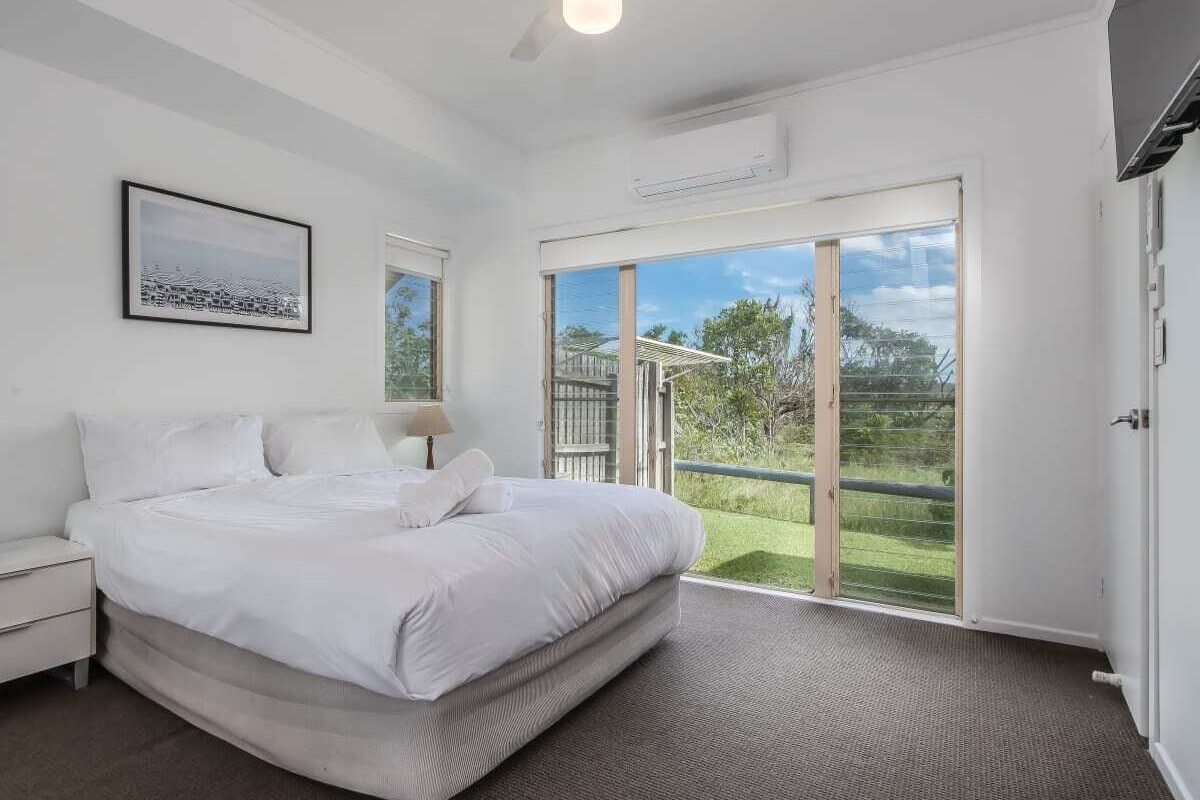 A bedroom with a large bed, a ceiling fan, and a sliding glass door leading to a balcony.