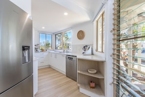 A modern kitchen with stainless steel appliances, white cabinetry, and a large window providing natural light. - Hastings Cove Waterfront Holiday Apartments (Hastings Point)