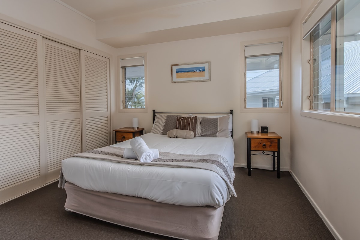 A bedroom with a bed, two bedside tables, a window, and a ceiling fan.