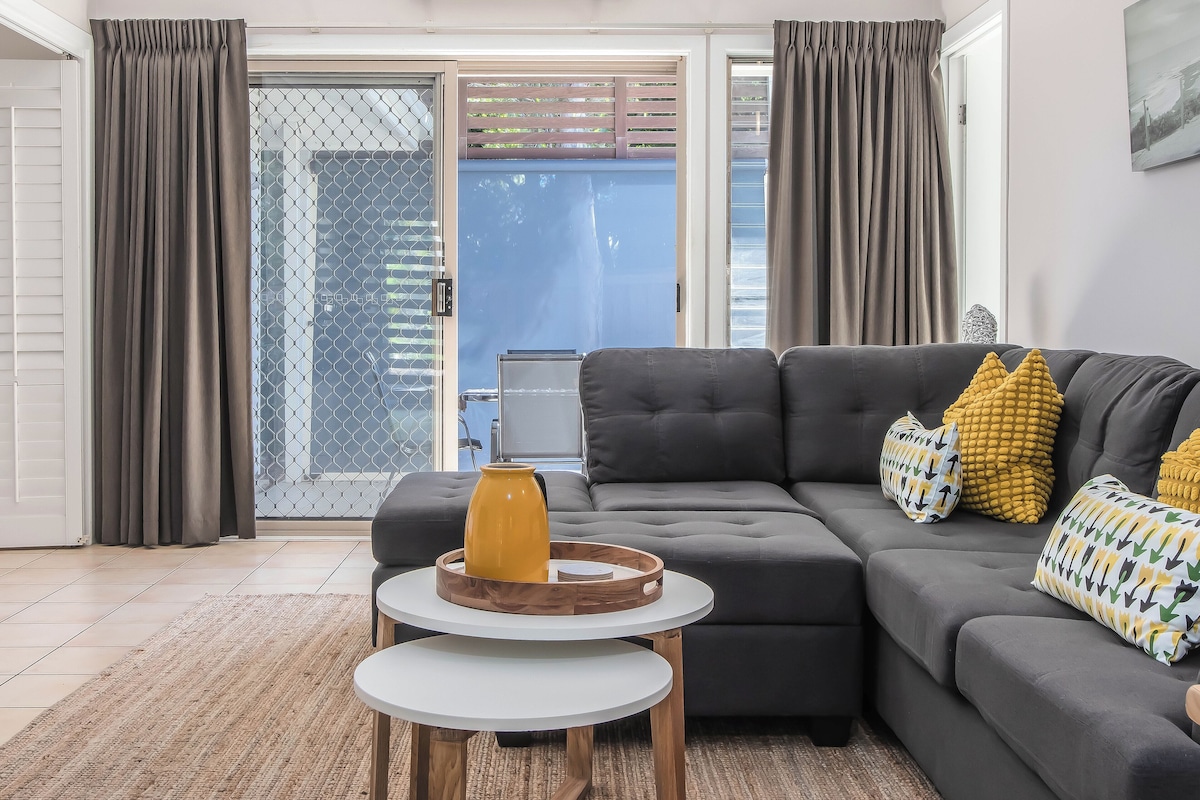 A modern living room with a sectional sofa, a coffee table, and a view through a glass door to the outside.