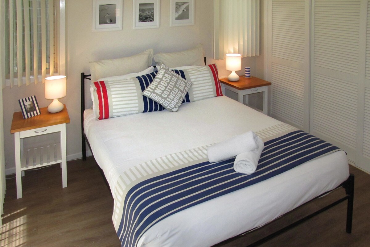 A neatly made bed with striped bedding, two bedside tables with lamps, and a framed picture on one table.