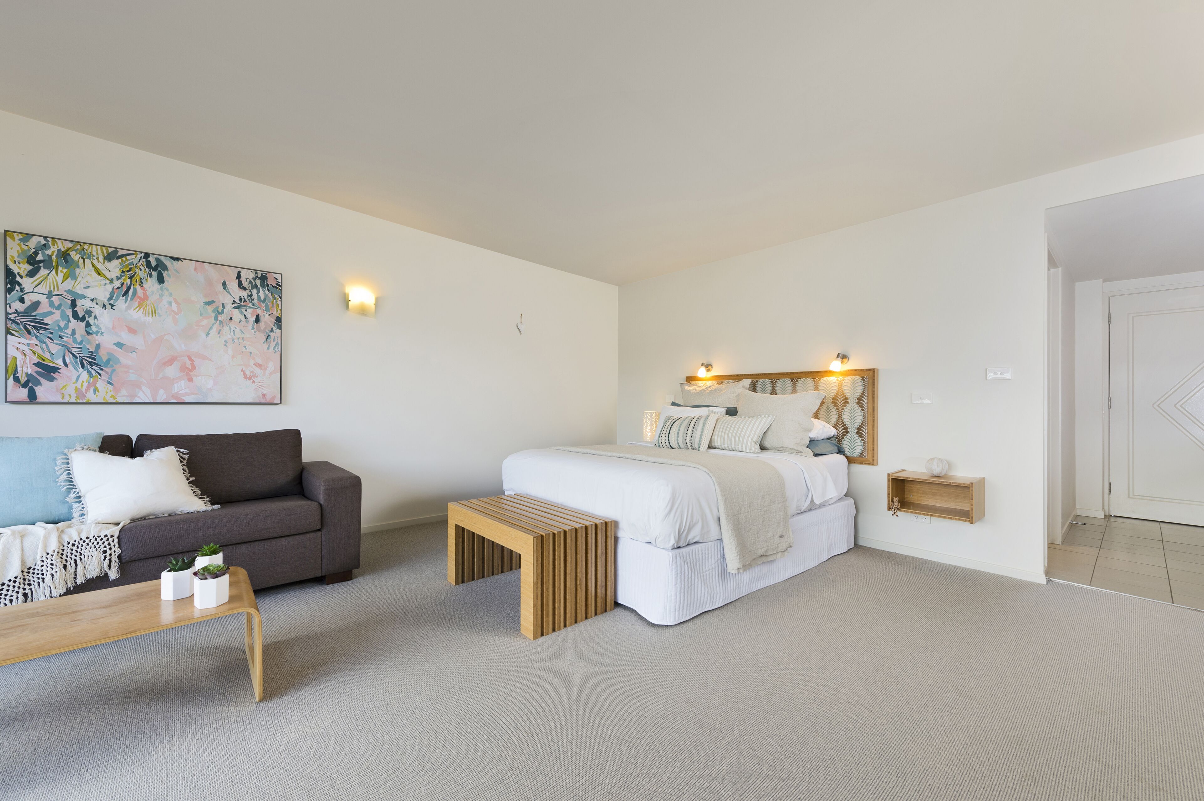 Un dormitorio moderno con cama, sofá, una mesita de centro y un cuadro en la pared.