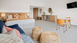 Une chambre d’hôtel moderne avec un grand lit, un bureau avec une chaise et un téléviseur fixé au mur.