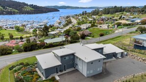 Un bâtiment moderne doté d’un toit plat, situé près d’une route et d’un port de plaisance où sont amarrés des bateaux.