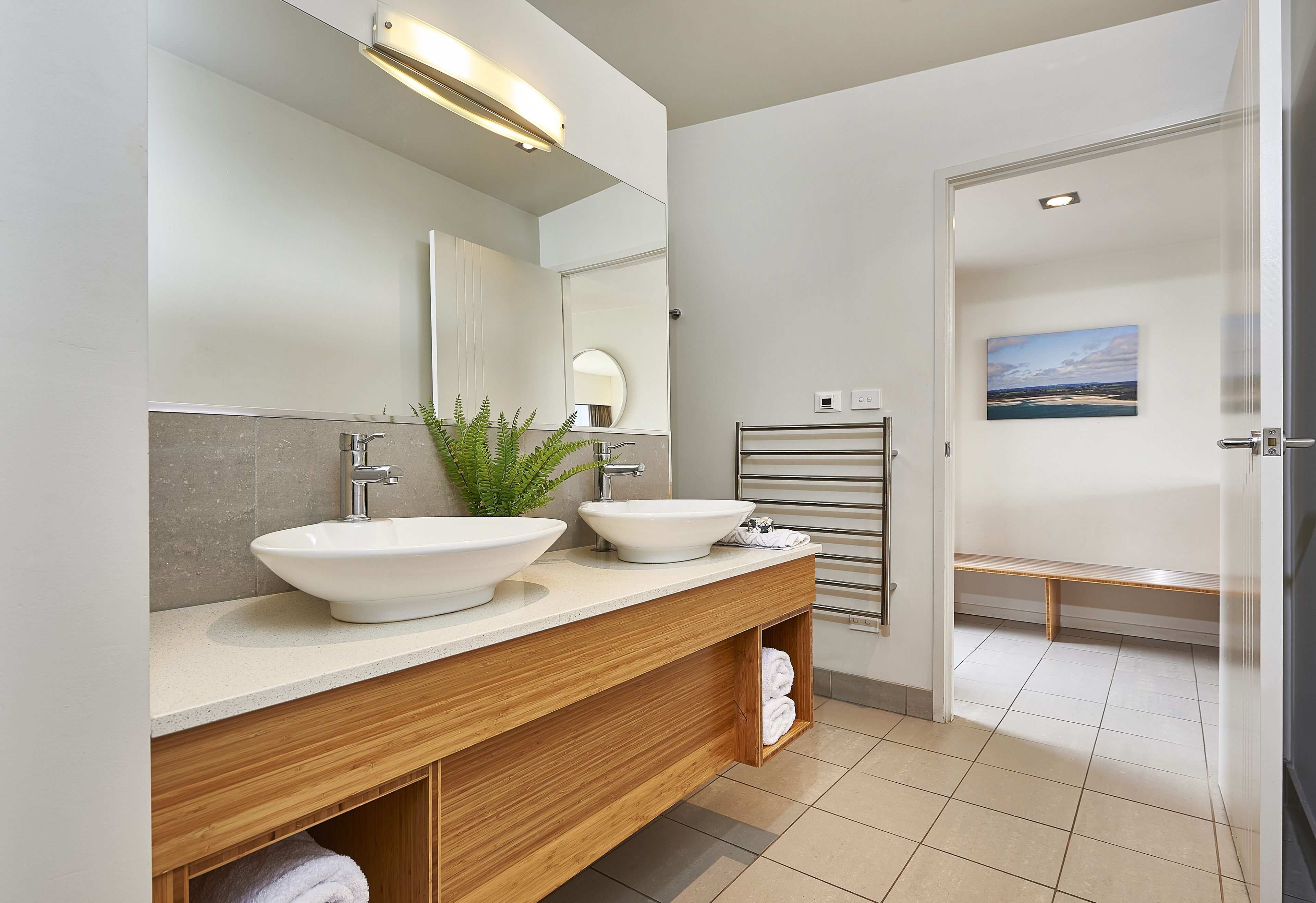 A modern bathroom with two sinks, a large mirror, and a towel rack.