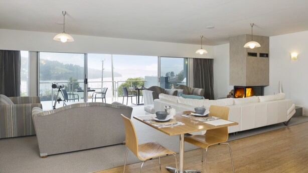 Un salon moderne doté d’une cheminée, d’un coin repas et de grandes fenêtres offrant une vue sur l’extérieur.