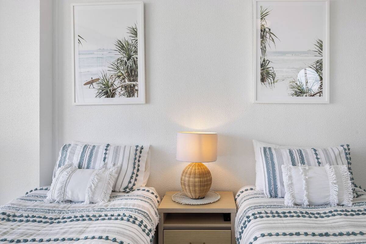 A bedroom with two beds, a nightstand with a lamp, and two framed pictures on the wall.
