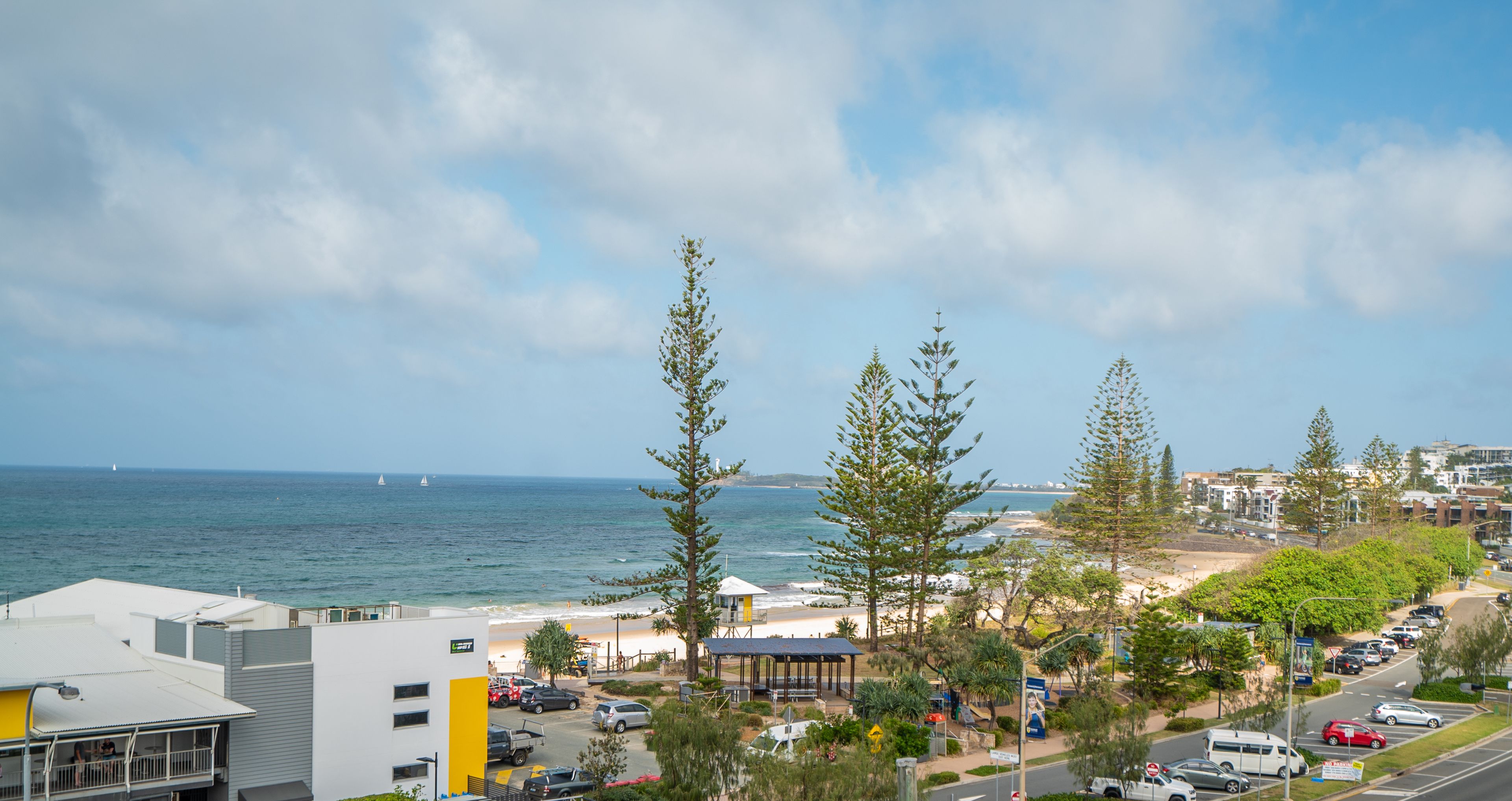 A coastal view with a beach, parking area, and buildings.