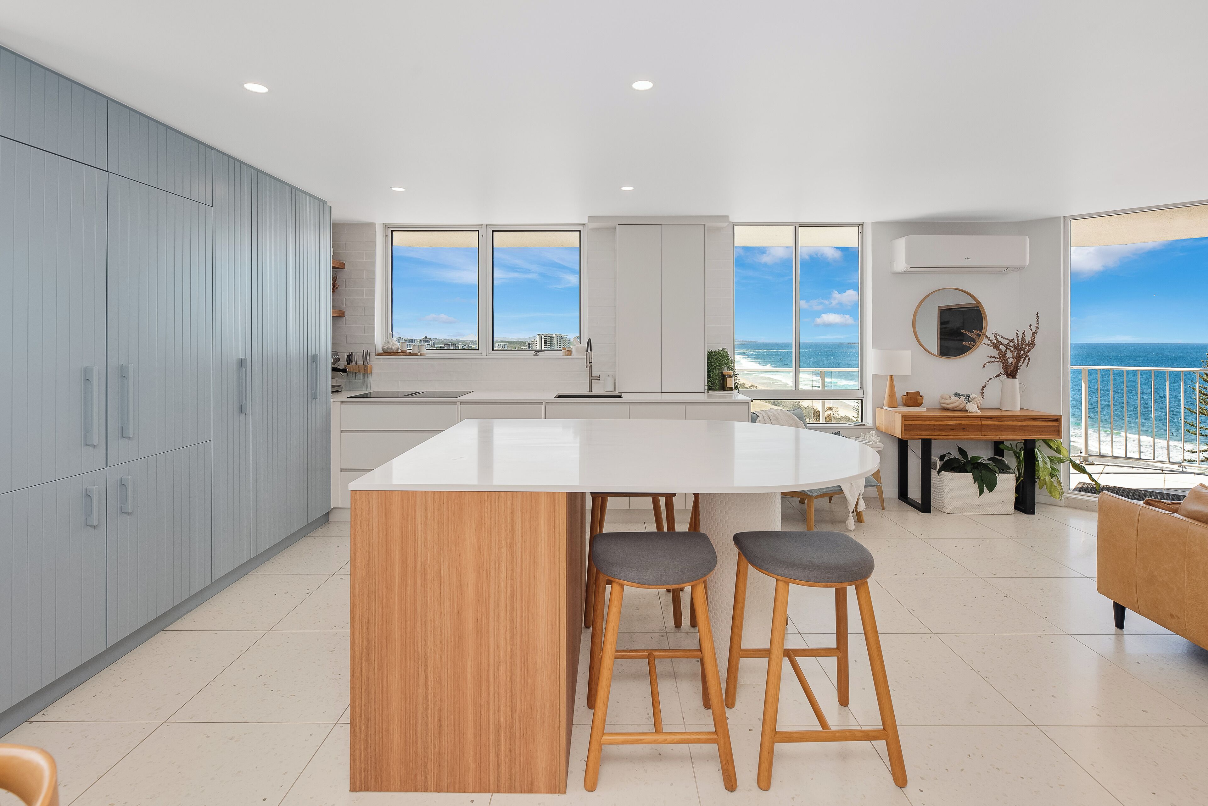 A modern kitchen with a large island, bar stools, and a view of the ocean.