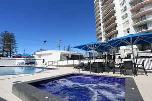 Zona de piscina de hotel con bañera de hidromasaje, sillones reclinables y sombrillas.
