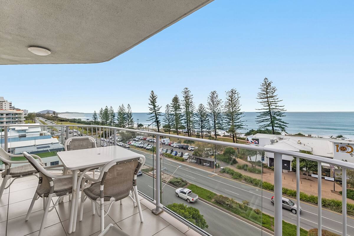 A balcony with a view of the road and ocean, featuring a table and chairs.