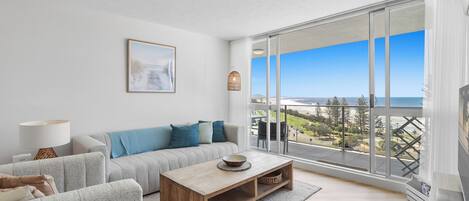 Uma sala de estar moderna com sofá, mesa de centro e uma janela grande com vista para a praia.