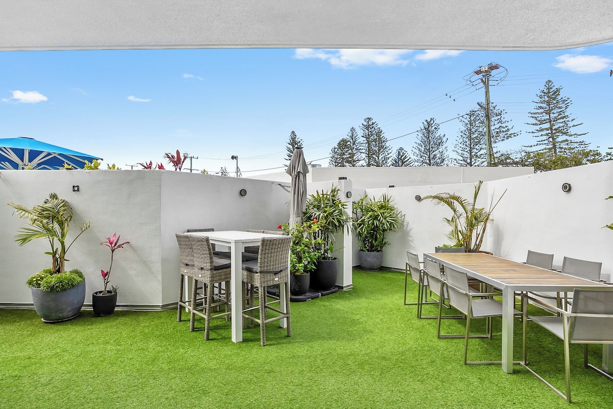 A patio with a white table and chairs, surrounded by potted plants and a green artificial turf.