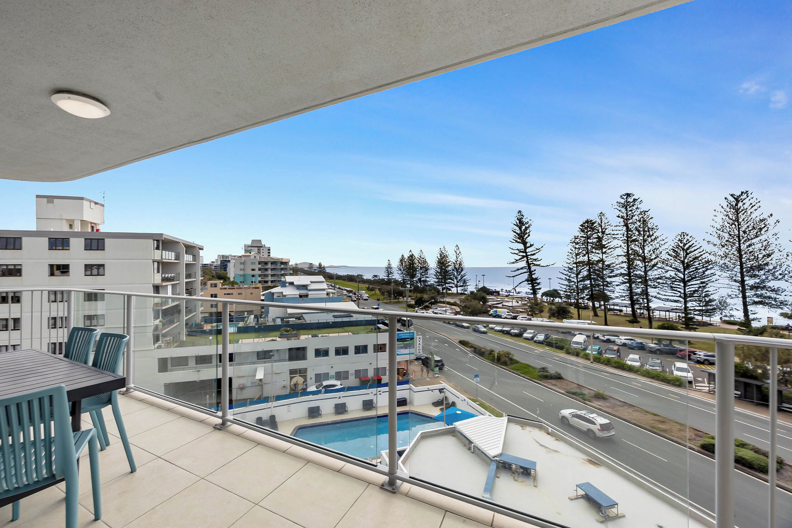 A balcony with a pool, outdoor seating, and a view of a road and buildings.