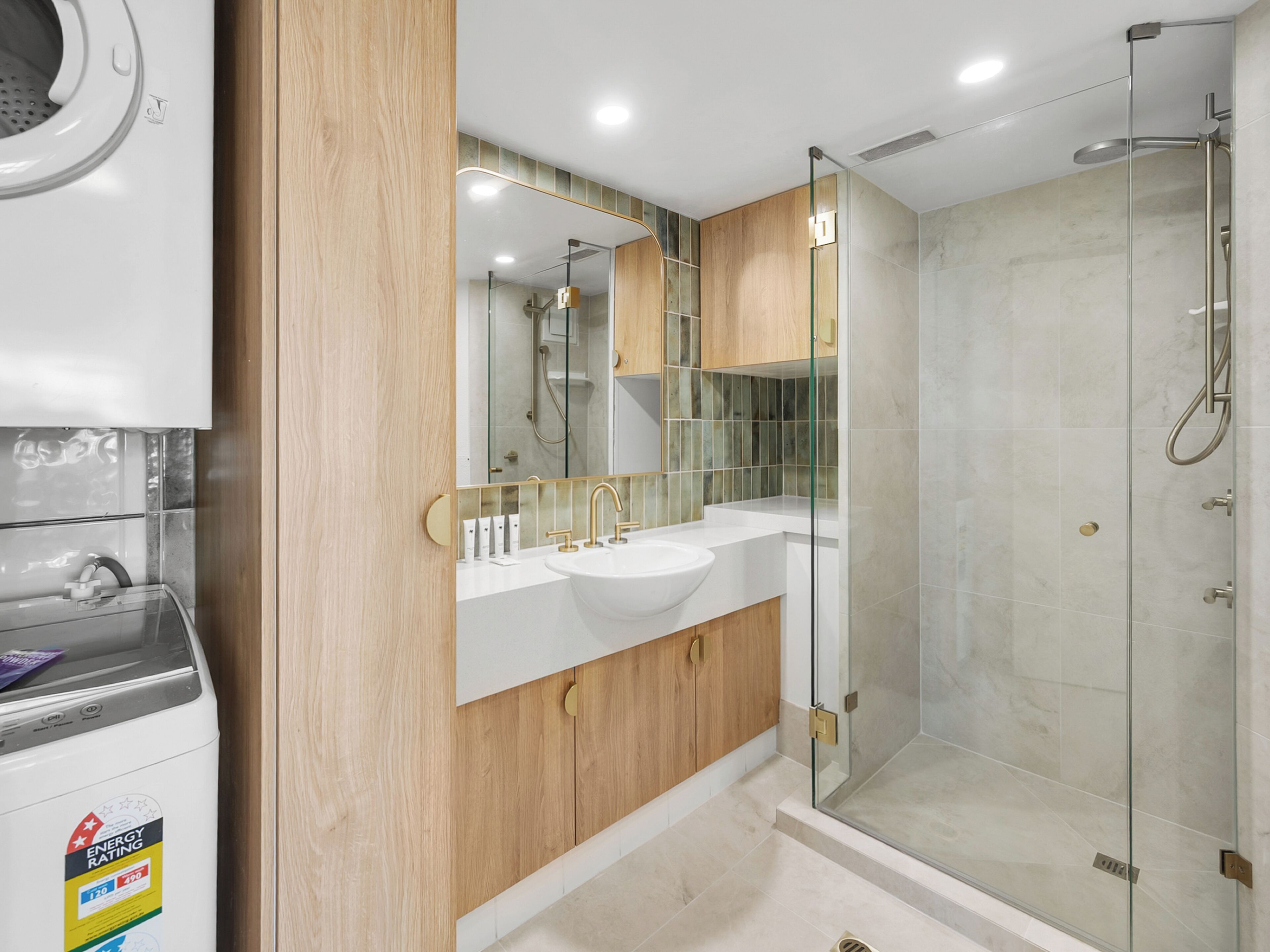 Un baño moderno con cabina de ducha de vidrio, un lavabo blanco y muebles de madera.