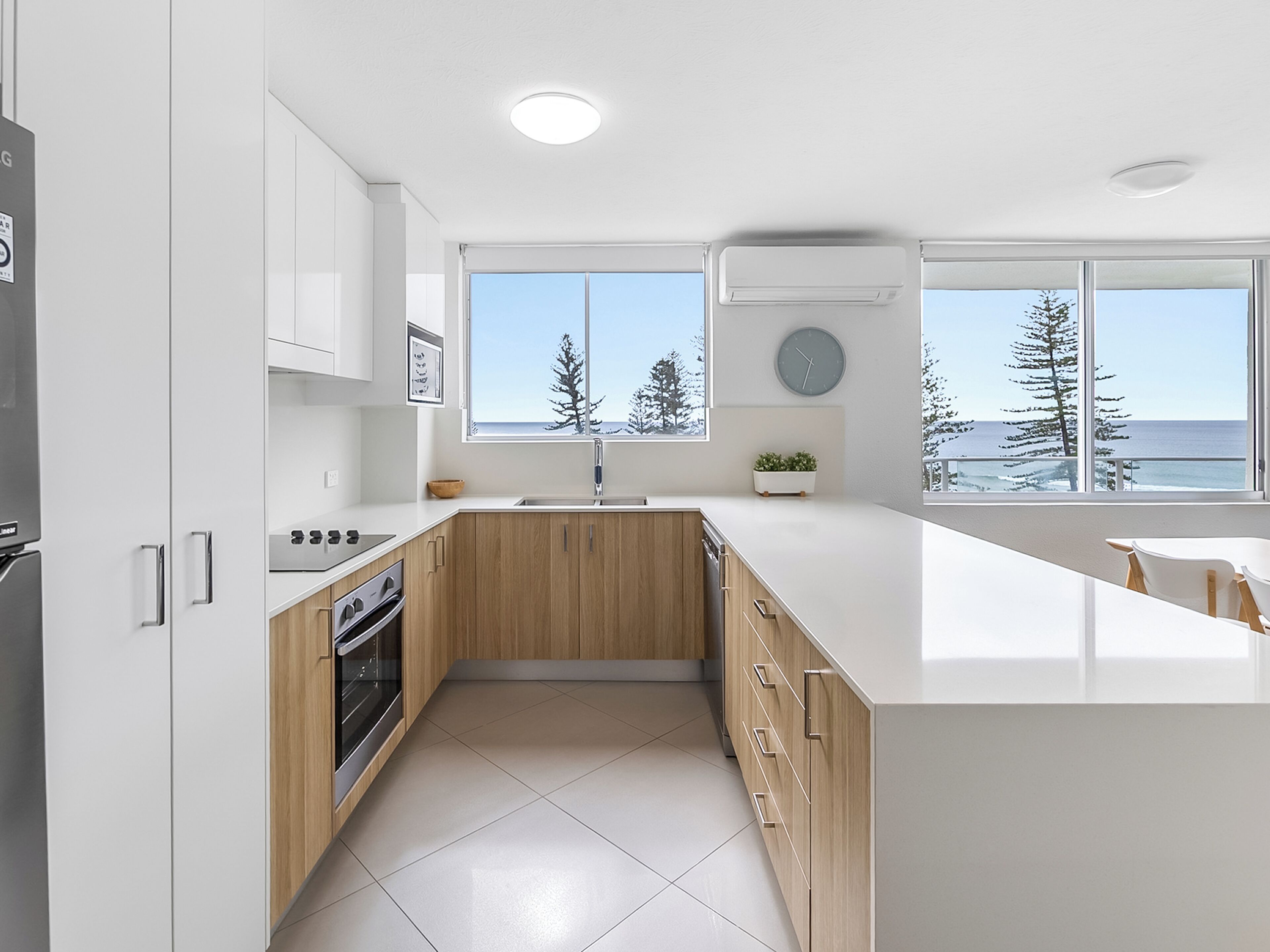 A modern kitchen with white cabinetry, a wooden countertop, and a view of the ocean through large windows.