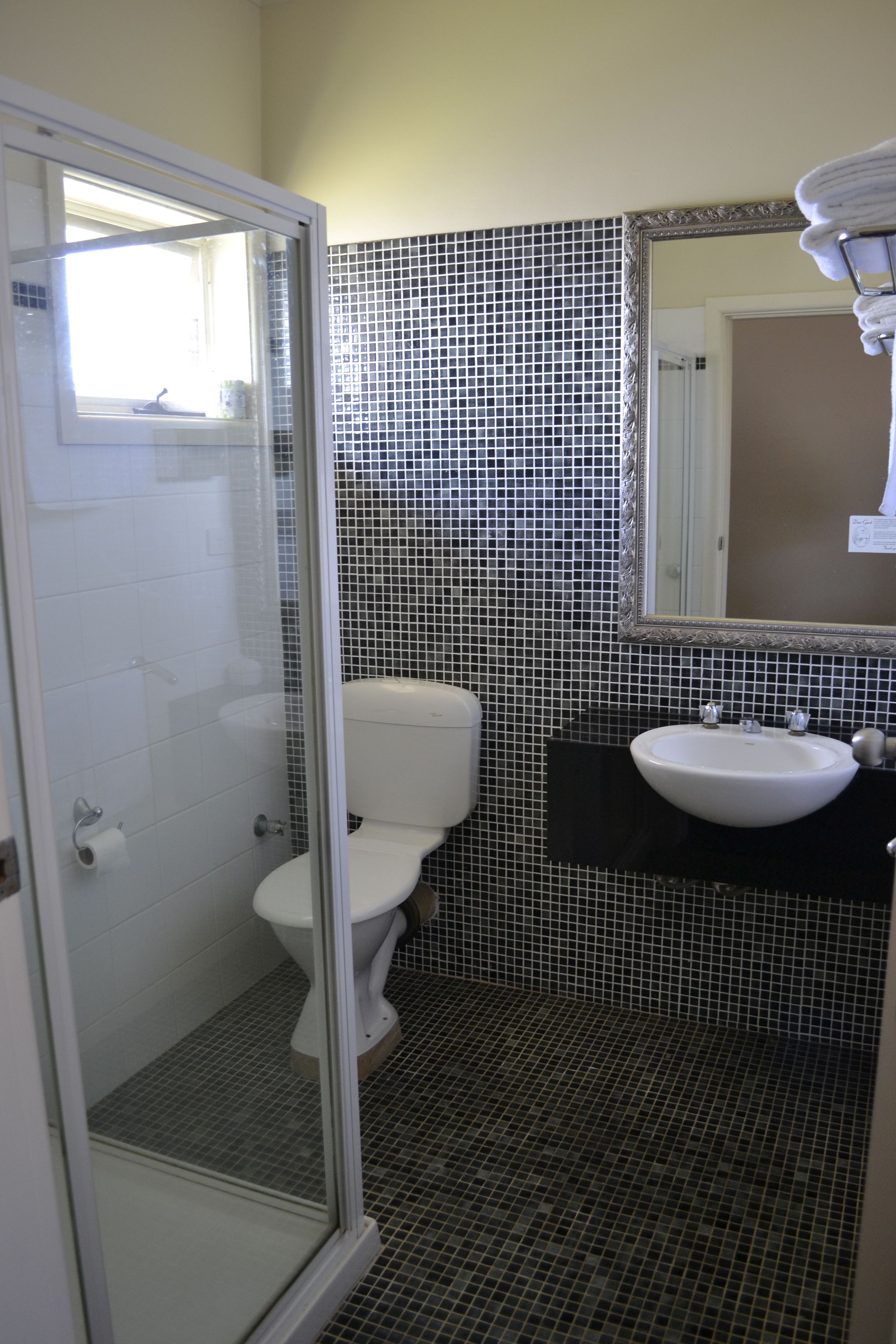 Un baño con cabina de ducha de vidrio, inodoro, lavamanos y salpicadero de azulejos.