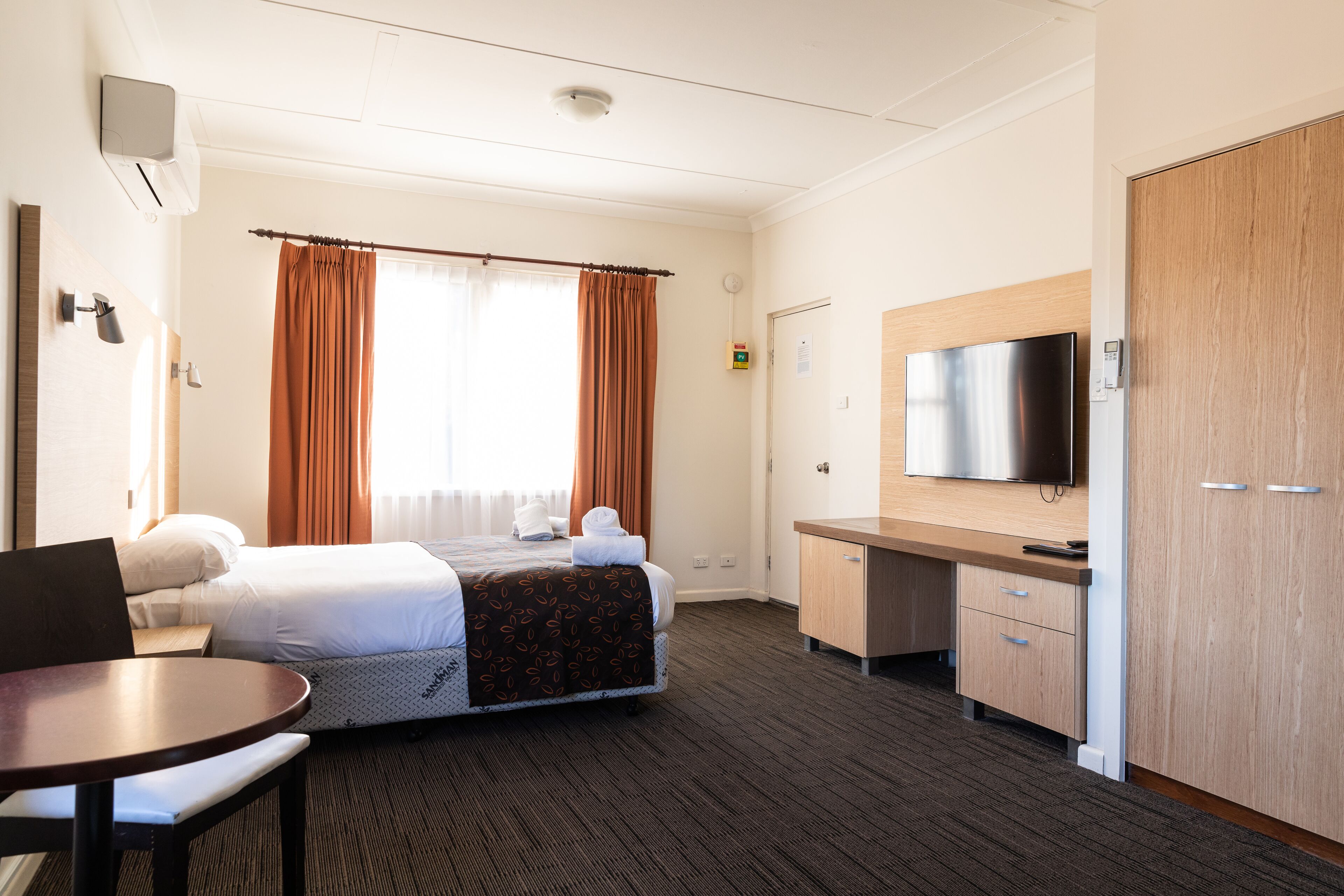 A hotel room with a bed, a desk, a television, and a wardrobe.