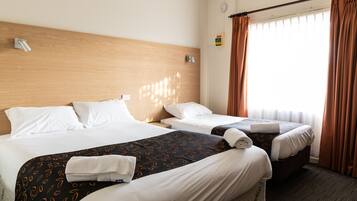 A hotel room with two beds, a wooden headboard, a window with curtains, and a small wall clock.