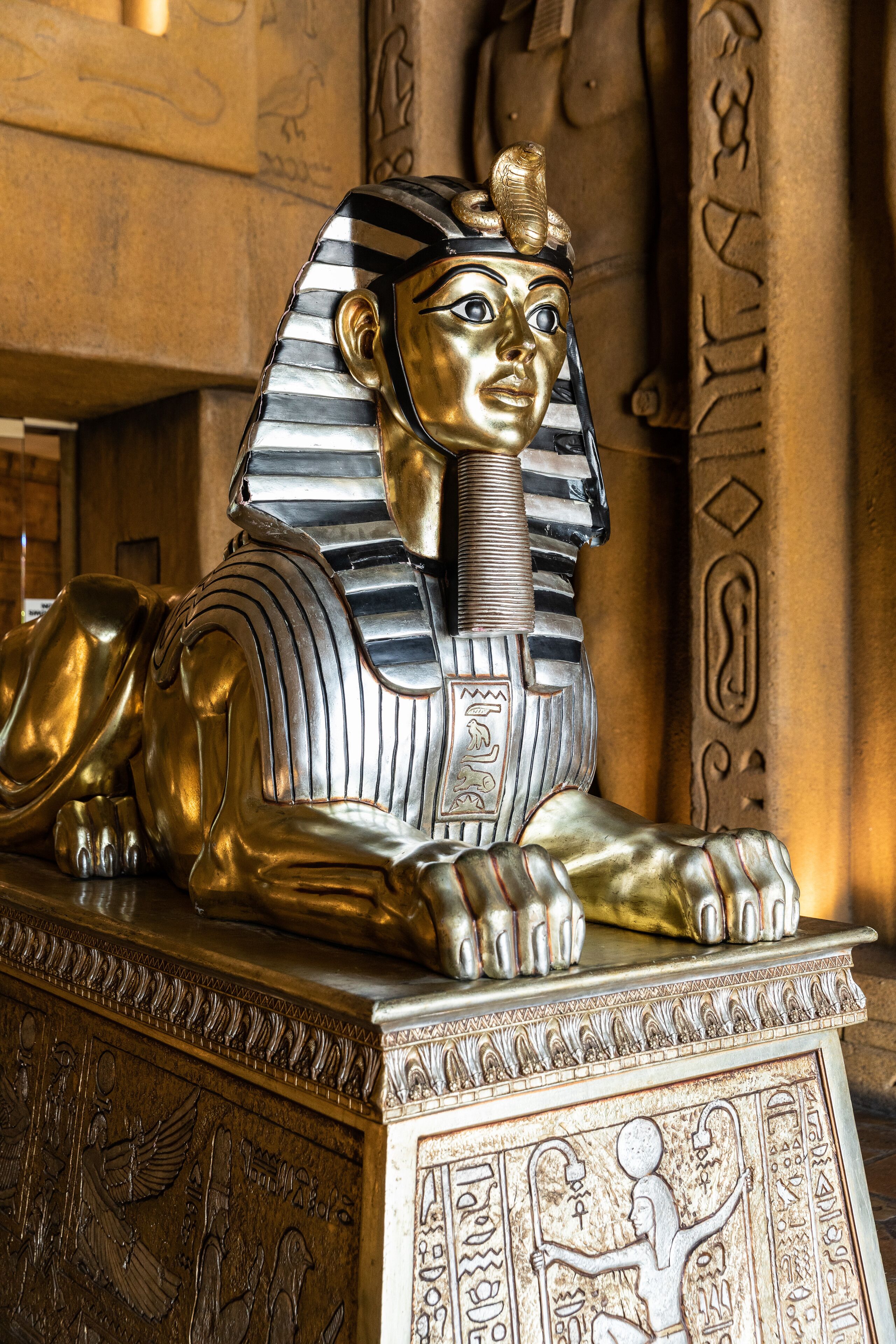 A golden statue of an Egyptian figure with a striped headdress, lying on a pedestal with hieroglyphic carvings.
