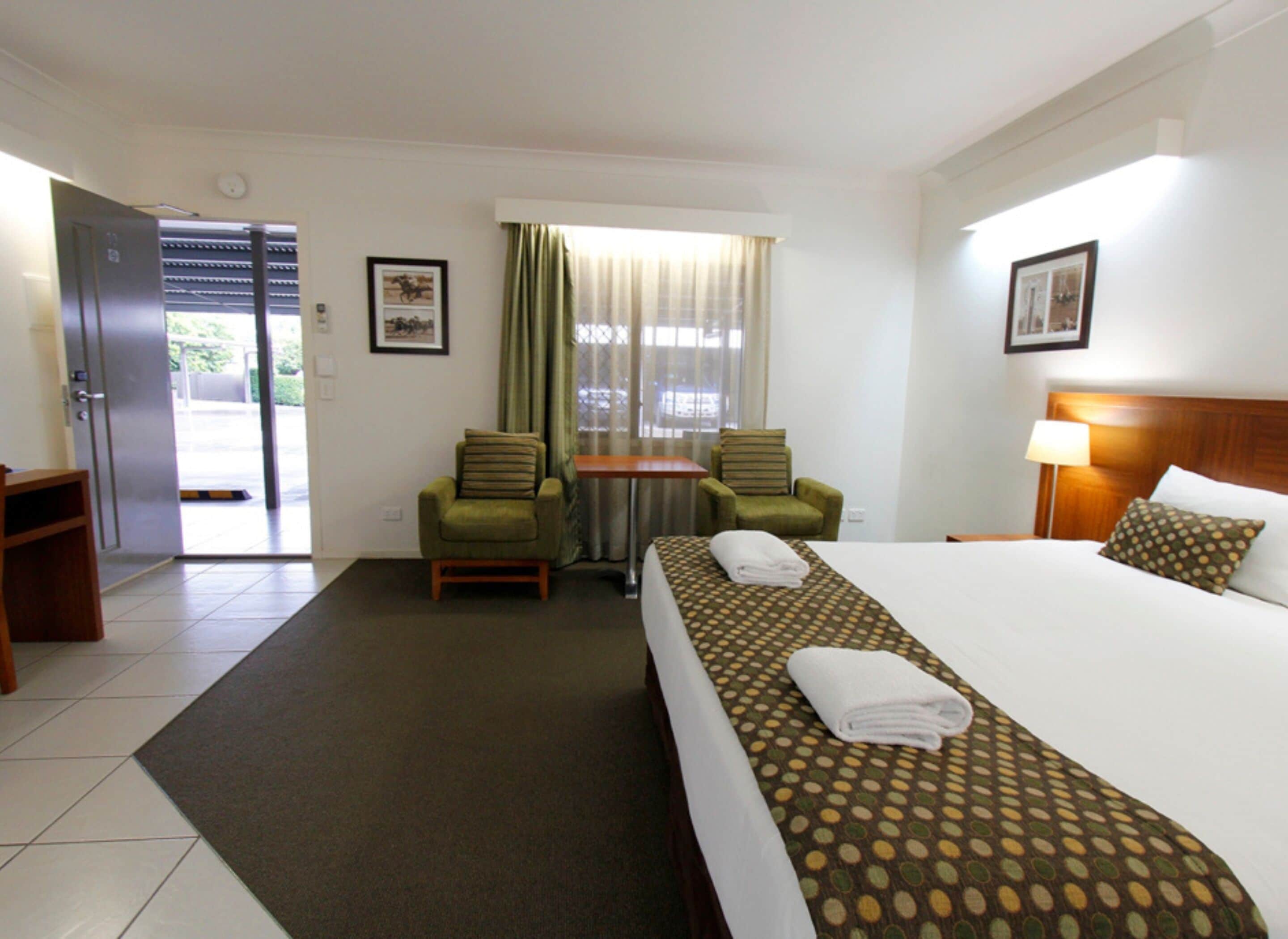 A hotel room with a bed, two chairs, a small table, and a window with curtains.