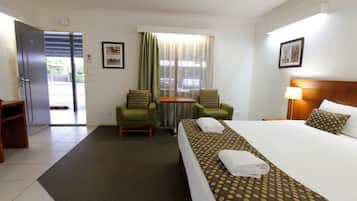 A hotel room with a bed, two chairs, a small table, and a window with curtains.
