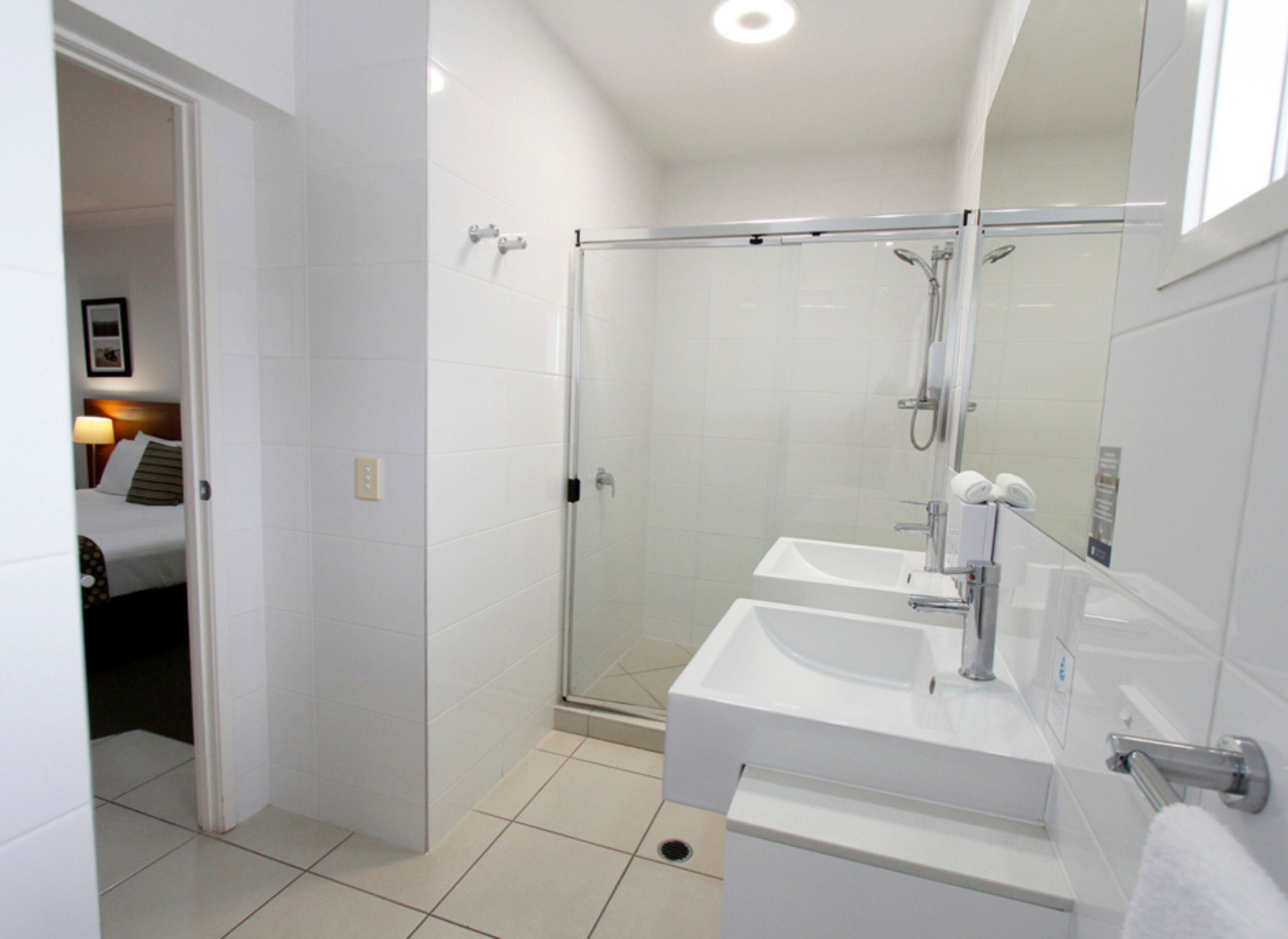 A modern bathroom with a glass shower enclosure, two sinks, and a large mirror.