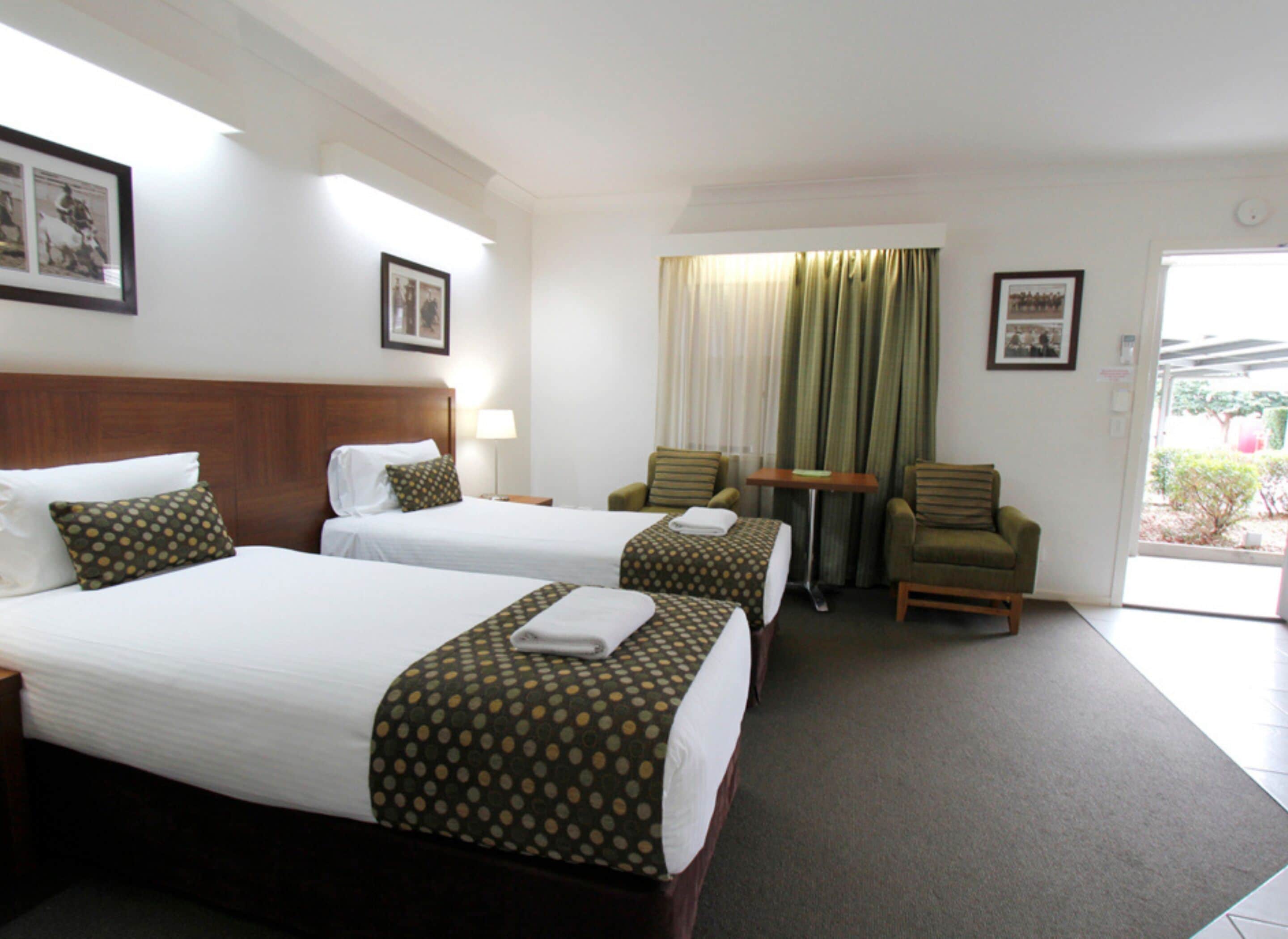 A hotel room with two beds, a small table, two chairs, and a window with curtains.
