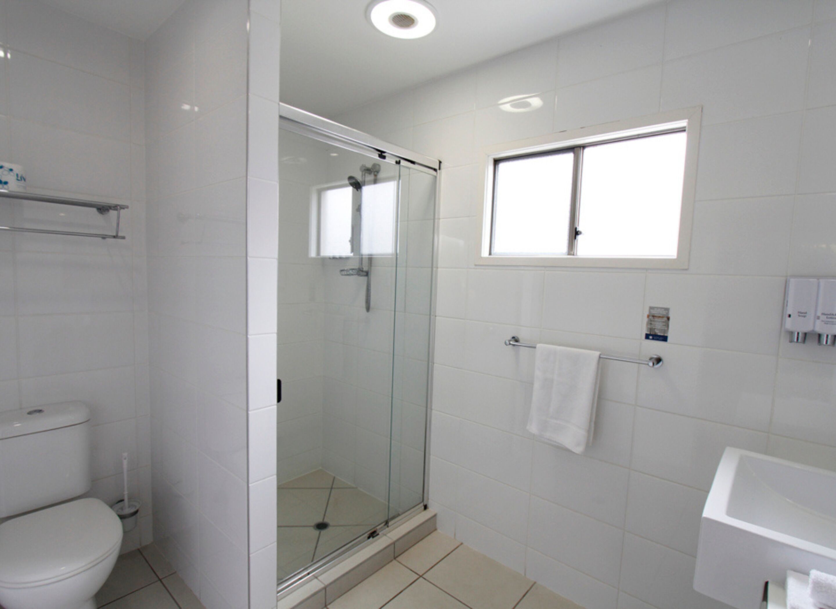Un baño moderno con ducha acristalada, inodoro, lavamanos y ventana.
