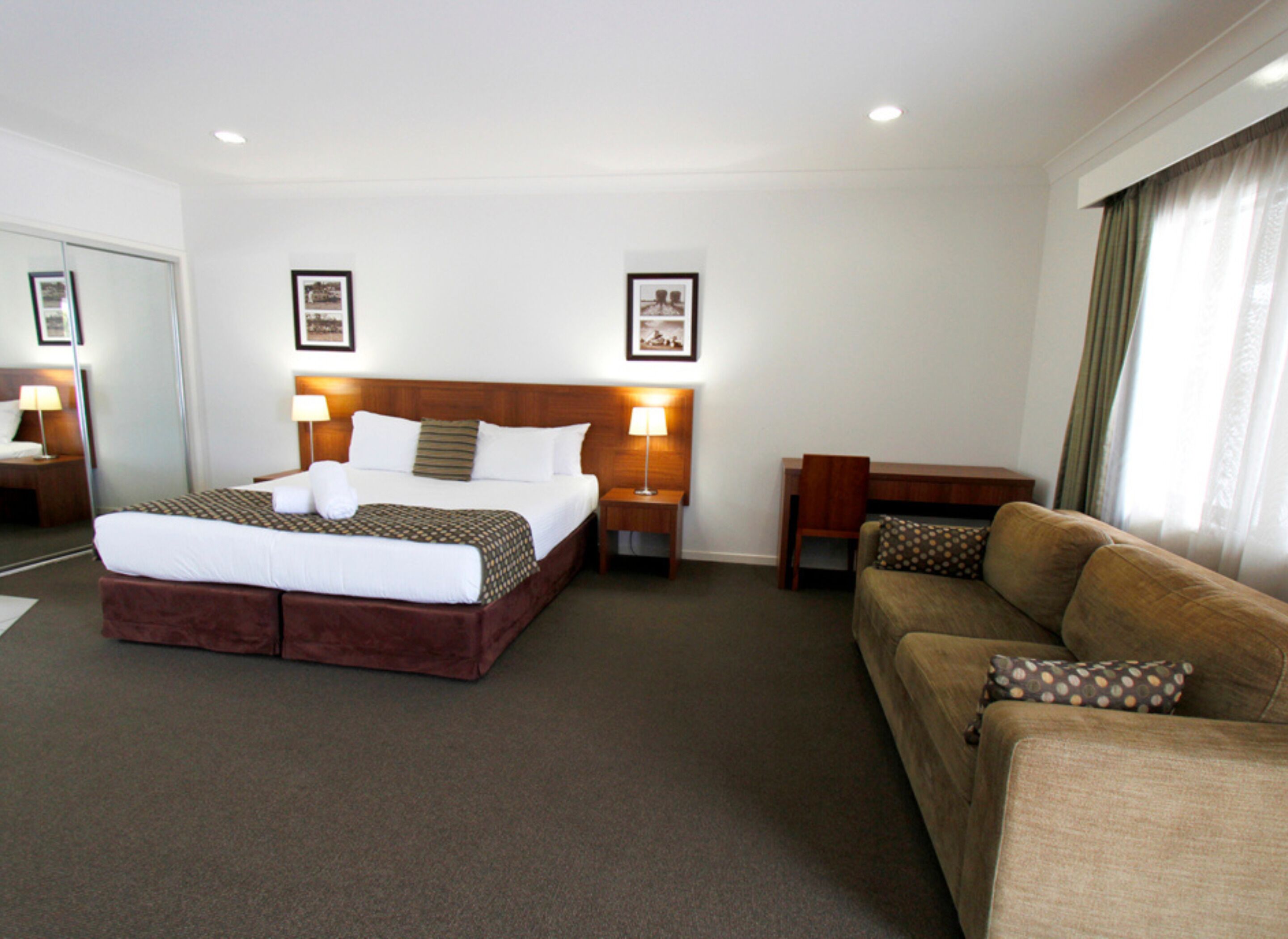 A hotel room with a large bed, a sofa, a desk, and two lamps.